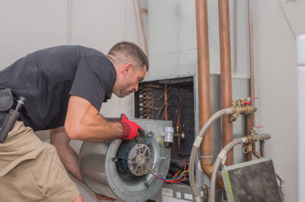 An HVAC technician repairs a furnace blower motor inside a residential heating system.
