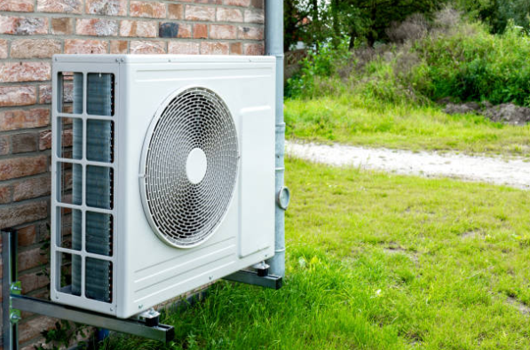 Outdoor air conditioning condenser unit installed against a brick wall beside a residential home.