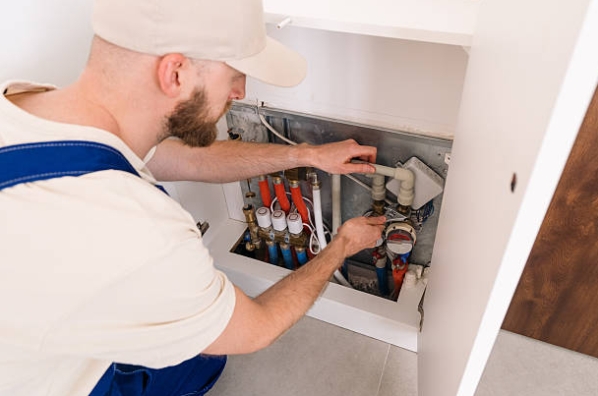 HVAC technician inspecting and adjusting plumbing and heating manifold connections inside a residential utility cabinet.
