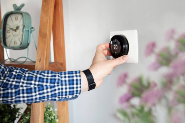 A person adjusts a smart thermostat mounted on a wall to set the indoor temperature to 70 degrees.