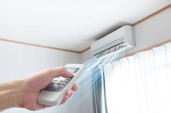 A person uses a remote control to adjust a wall mounted split air conditioner blowing cool air inside a room.